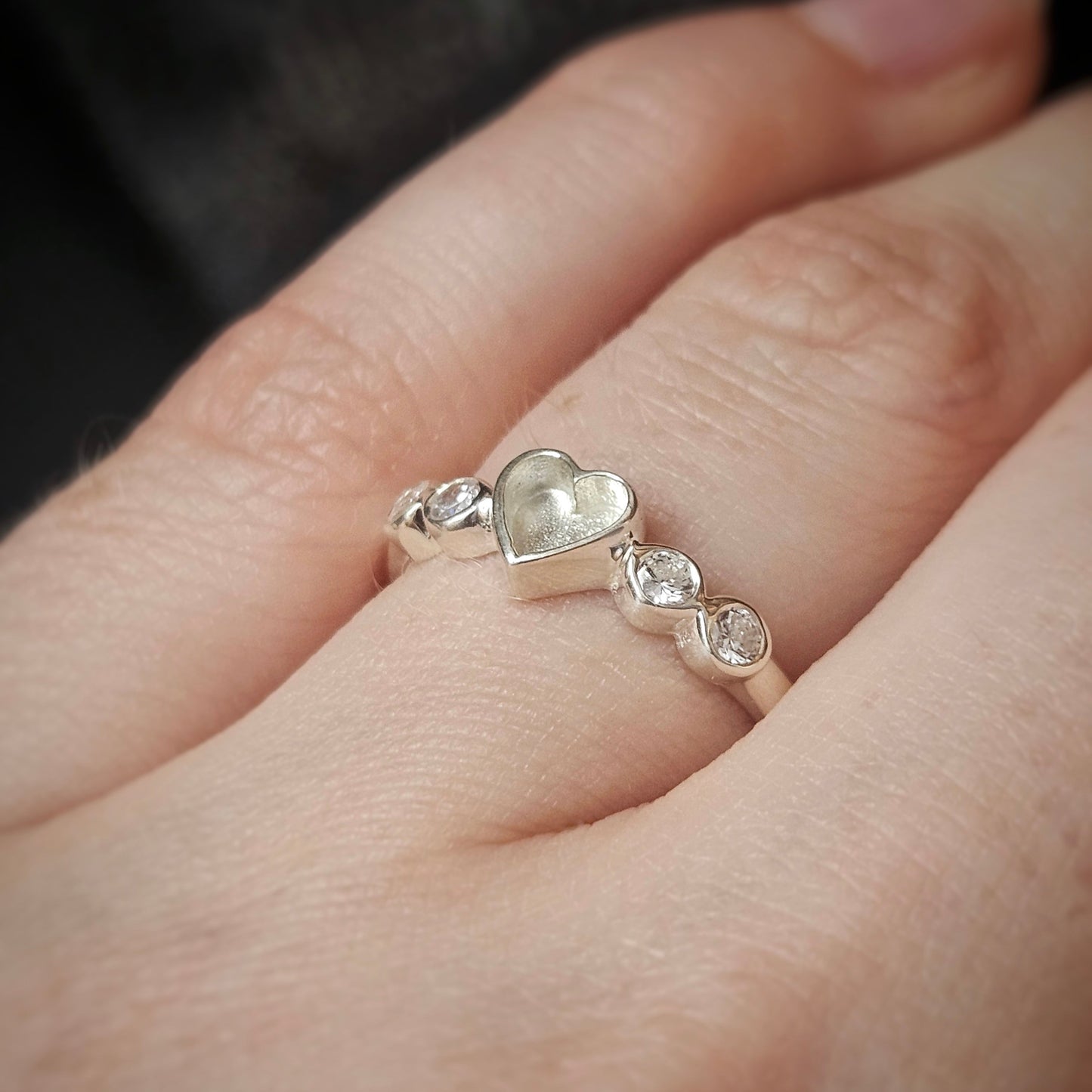 Silver ring with heart and diamond designs on a finger