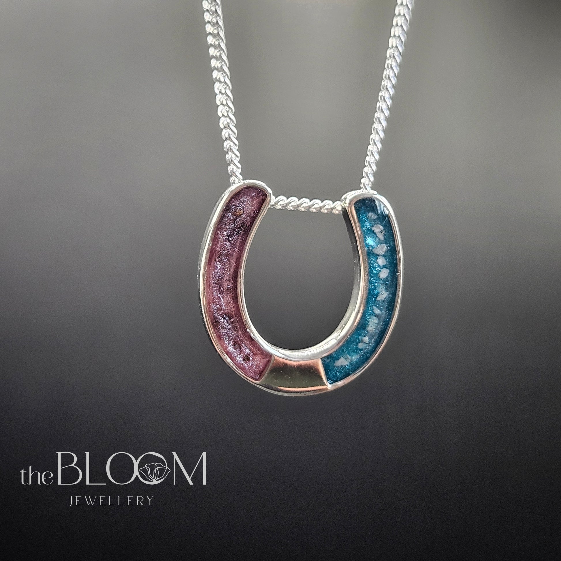 Horseshoe-shaped pendant with pink and blue colors on a chain against a dark background, branded 'the BLOOM JEWELLERY'.
