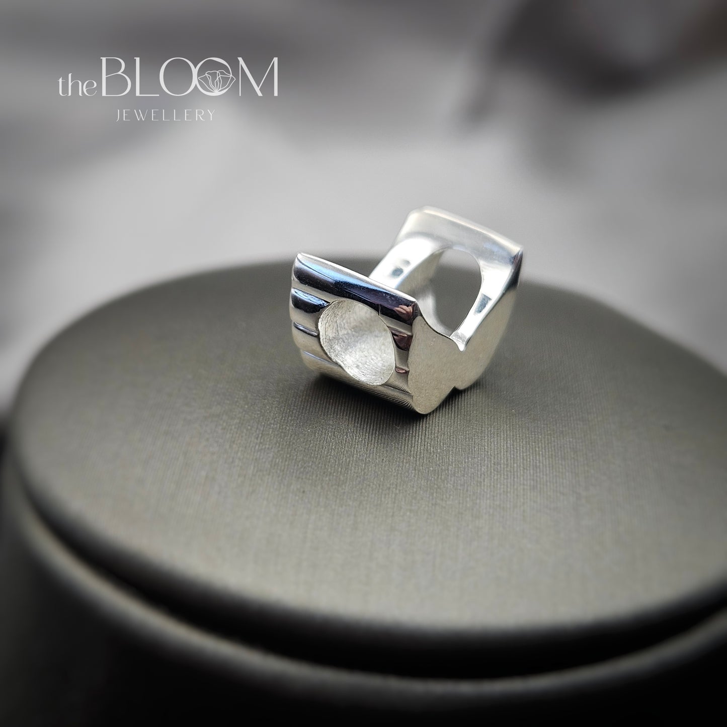 Silver ring on a gray surface with 'the BLOOM JEWELLERY' branding.