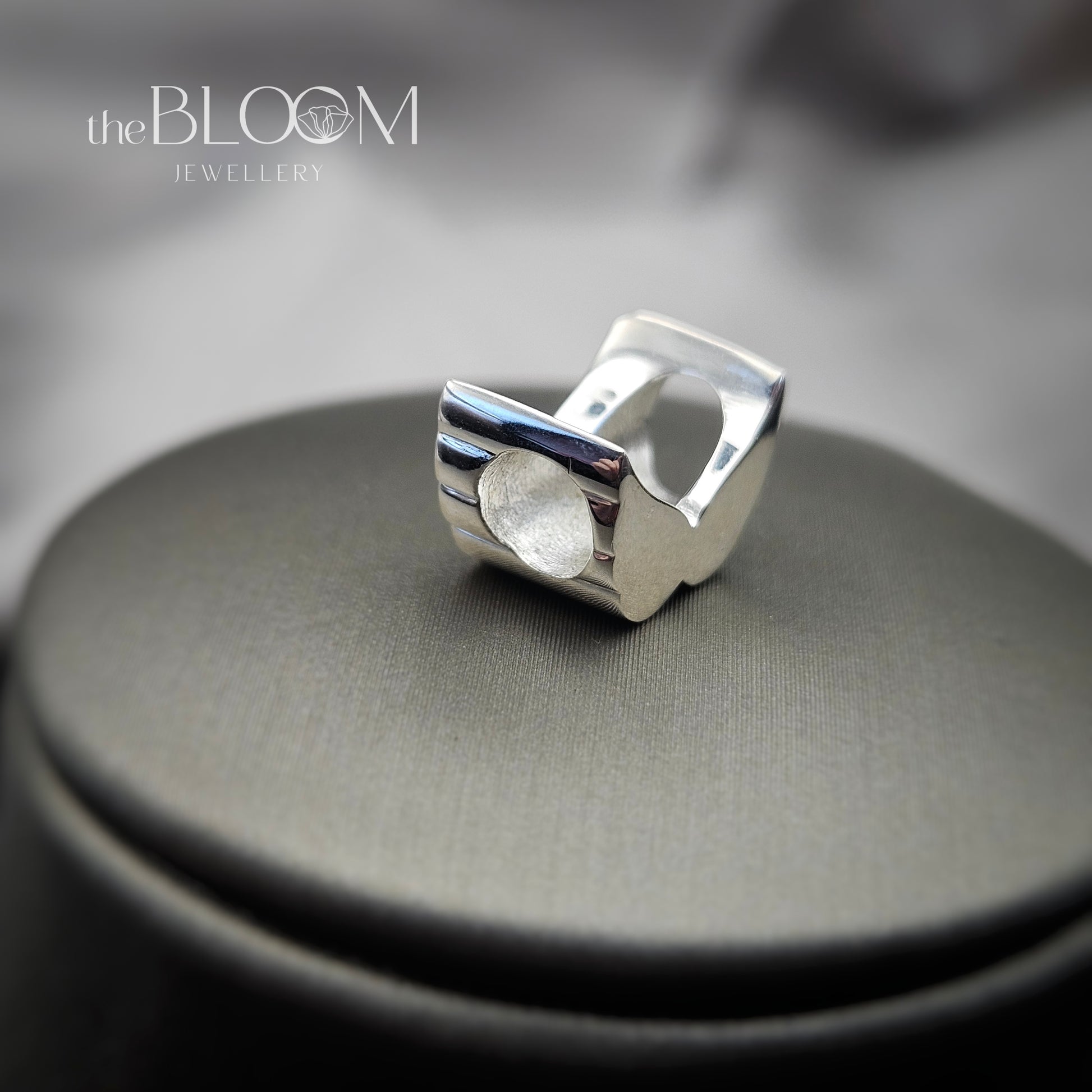 Silver ring on a gray surface with 'the BLOOM JEWELLERY' branding.