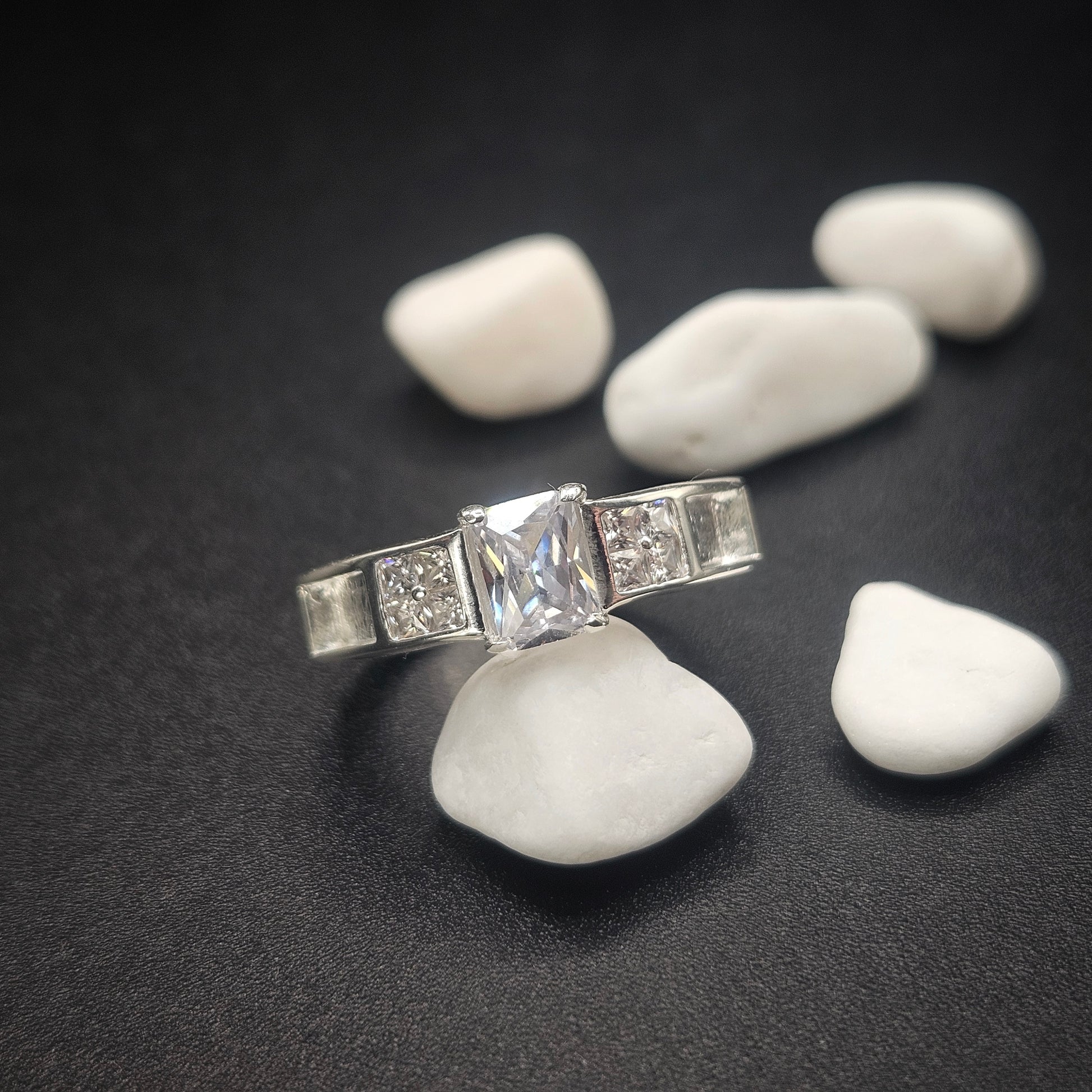 Silver ring with a large central gemstone on a dark surface with white stones.