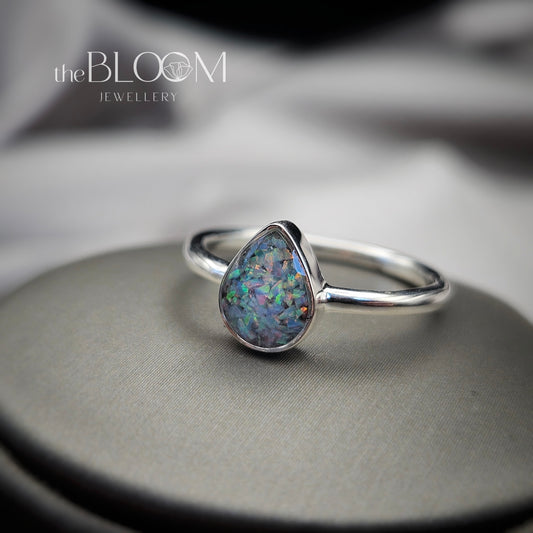 Silver ring with a teardrop-shaped opal stone on a gray surface, branded 'the BLOOM JEWELLERY'.