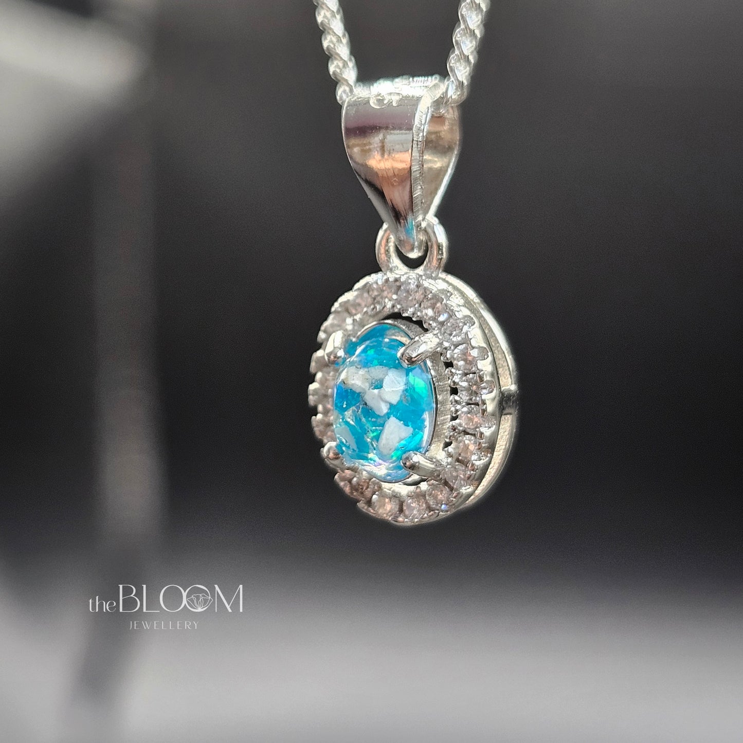 Silver pendant with a blue gemstone on a dark background, branded 'the BLOOM'.