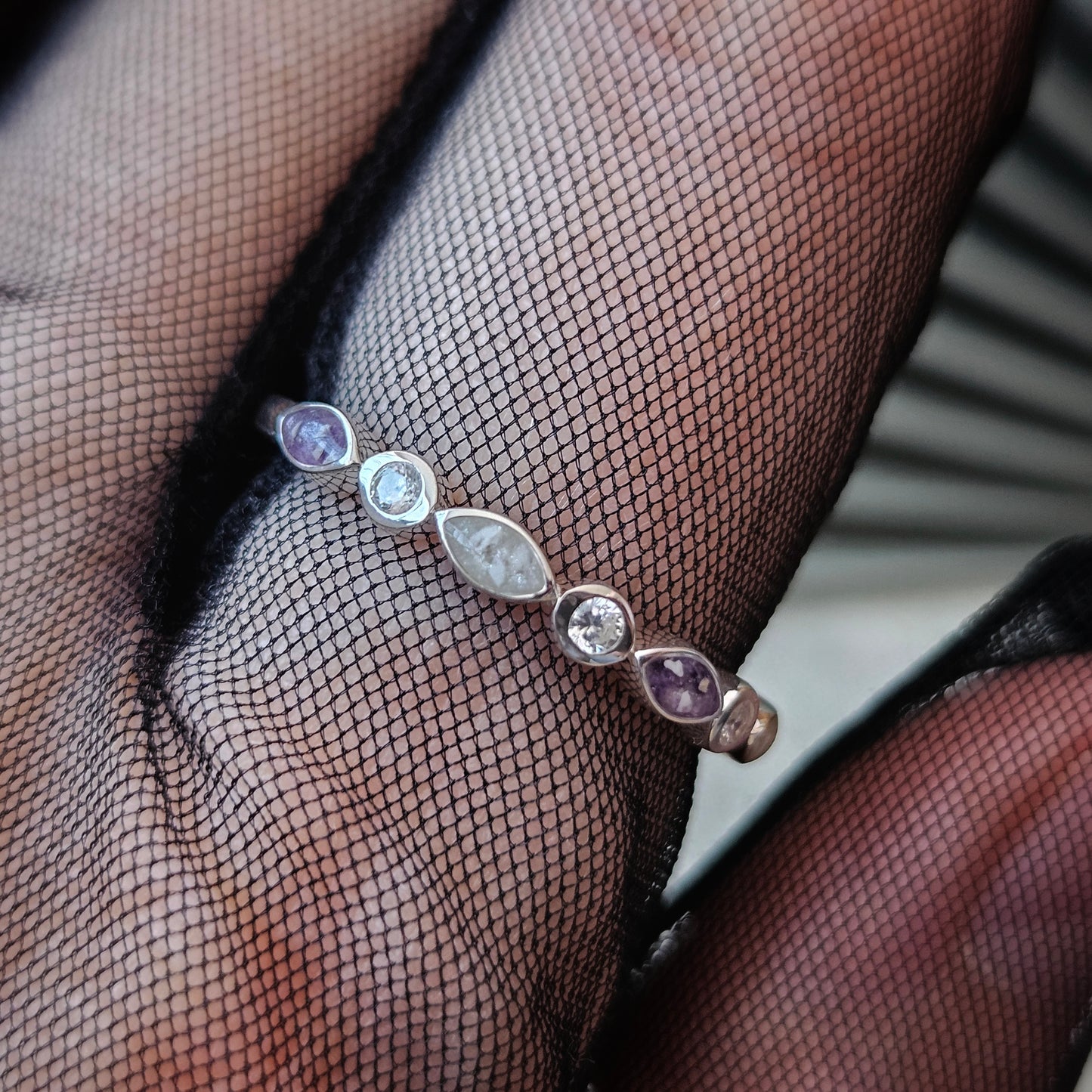 Silver bracelet with purple stones worn on a person's wrist against black fishnet stockings.