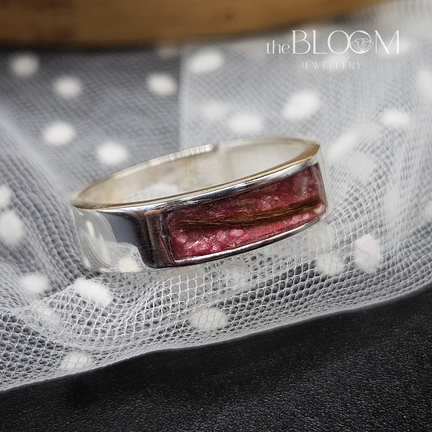 Silver ring with a red stone on a textured fabric background, branded 'the BLOOM JEWELRY'.