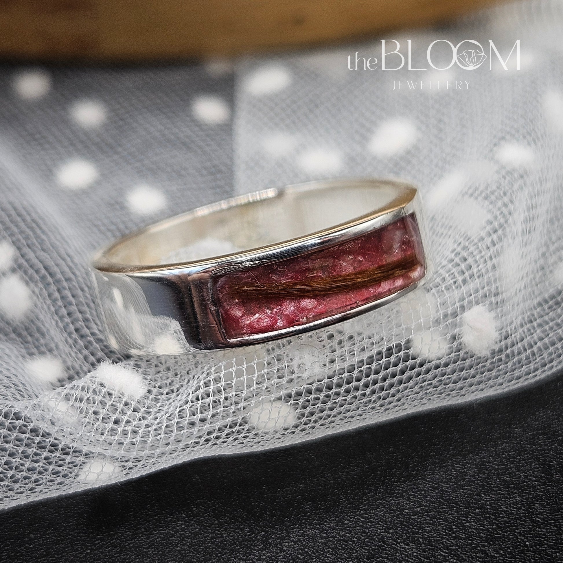Silver ring with a red stone on a textured fabric background, branded 'the BLOOM JEWELRY'.
