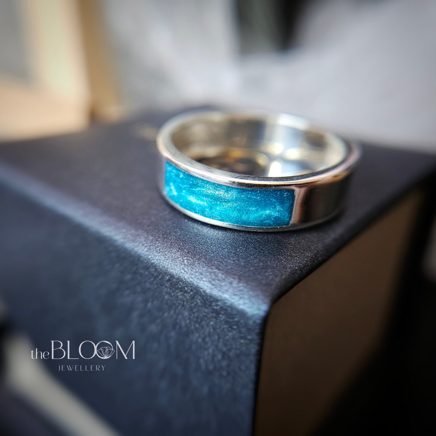 Silver ring with blue inlay on a dark surface, branded 'the BLOOM JEWELLERY'.