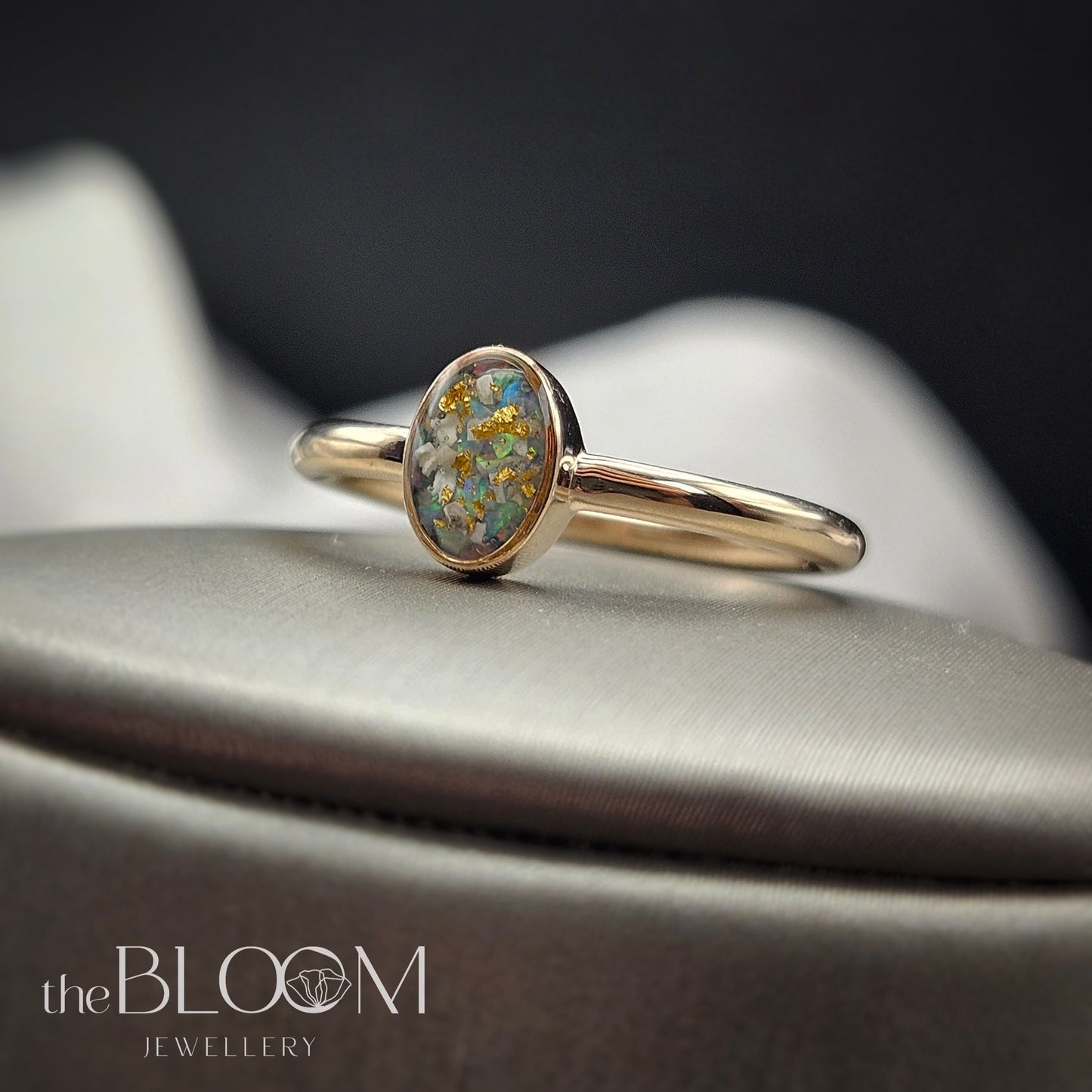 Gold ring with a central gemstone on a dark background, featuring 'the Bloom Jewellery' brand.