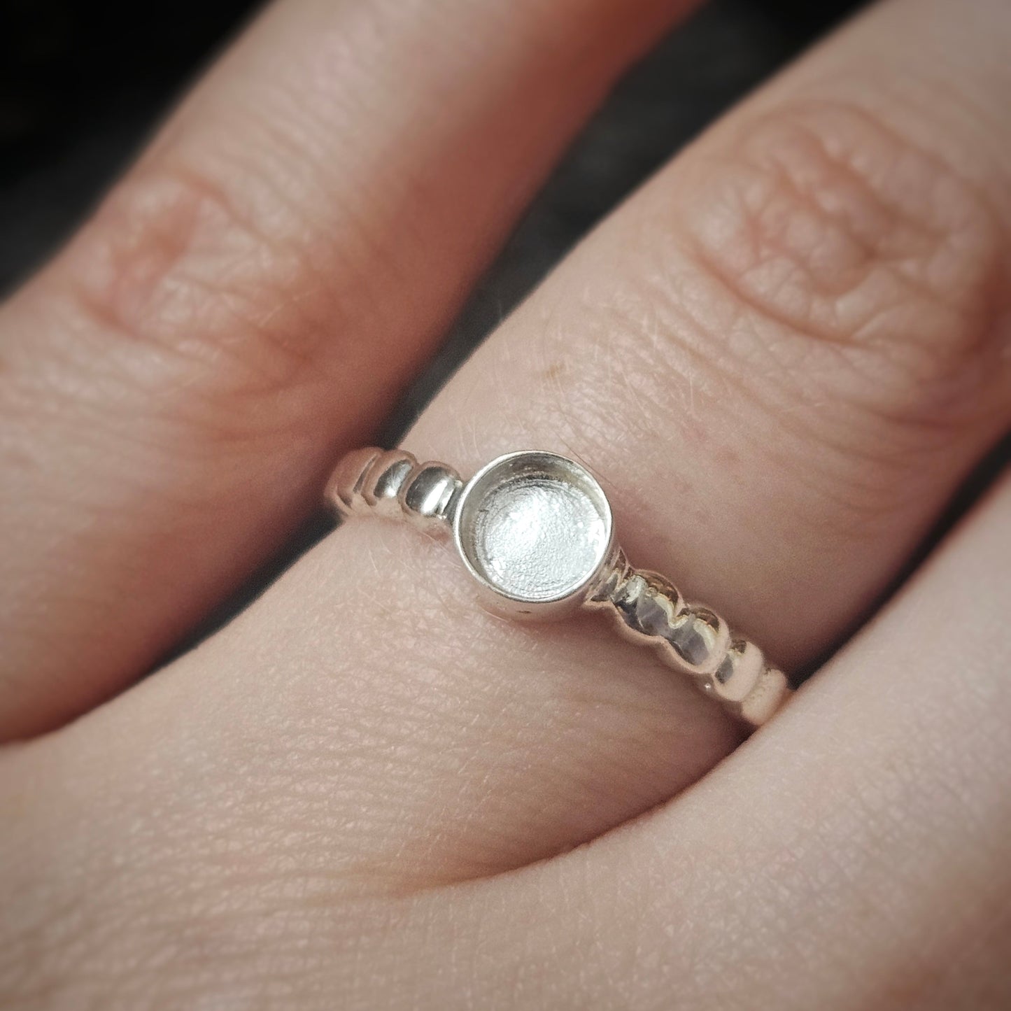 Silver ring with a textured band worn on a finger against a neutral background