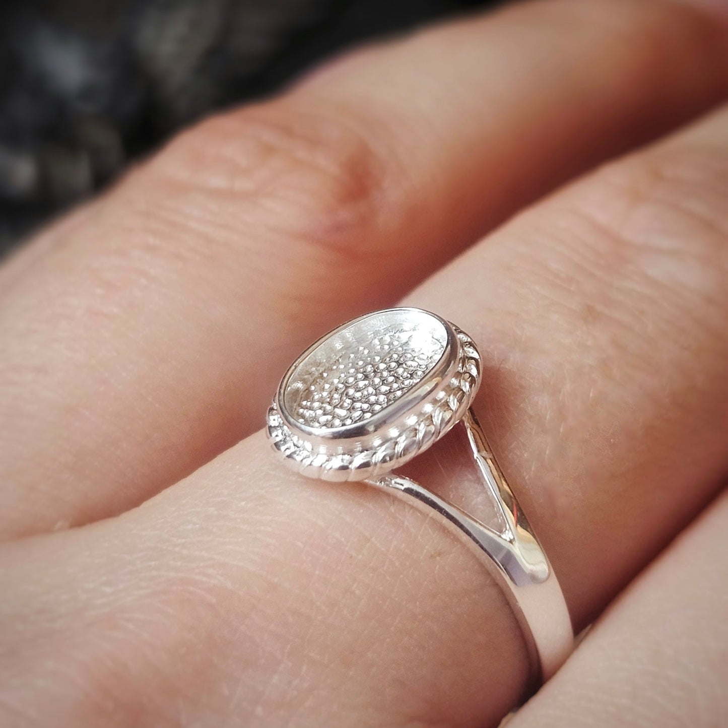 Silver ring with textured design on a finger against a blurred background