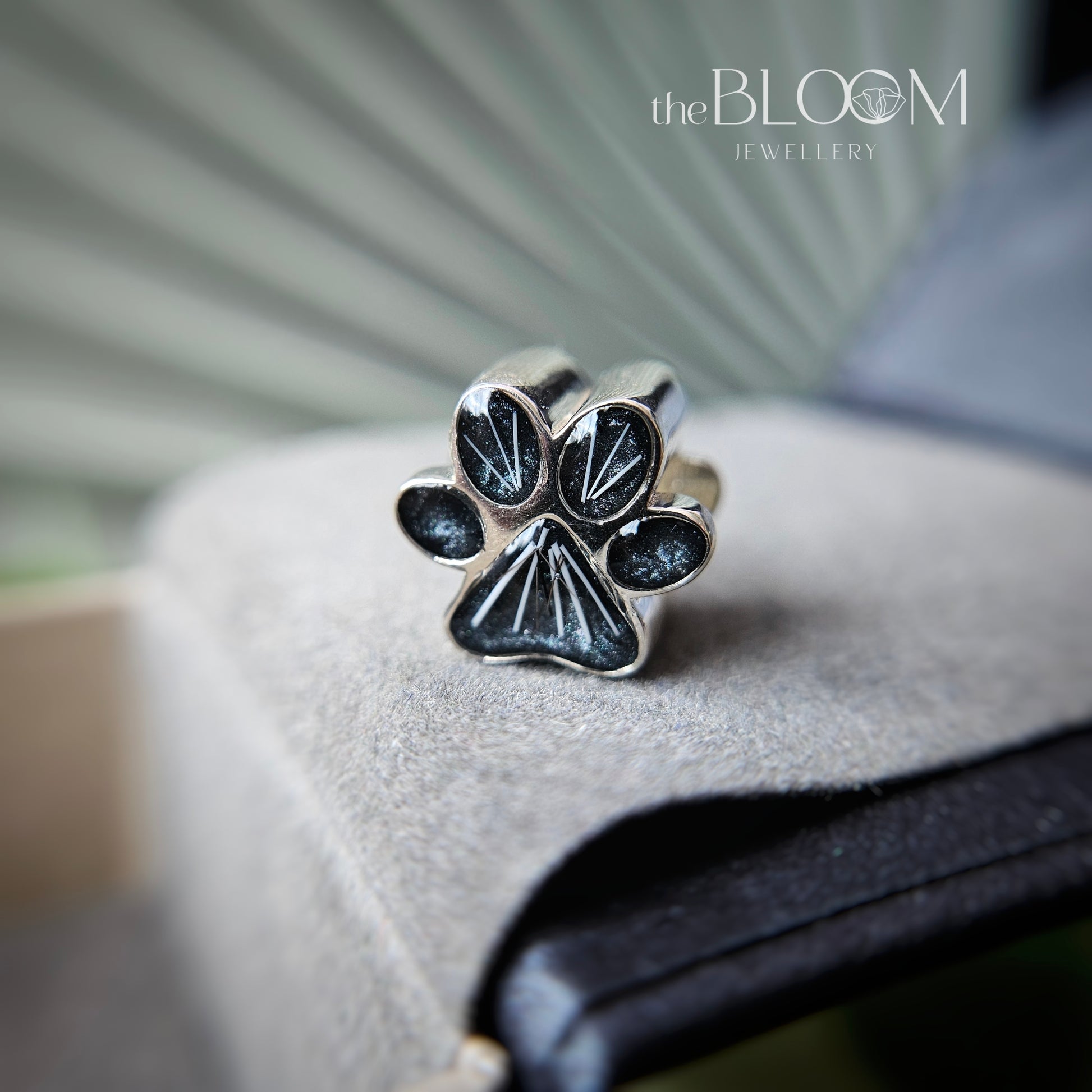 Silver paw print charm with black accents on a textured surface, branded 'theBLOOM Jewellery'.