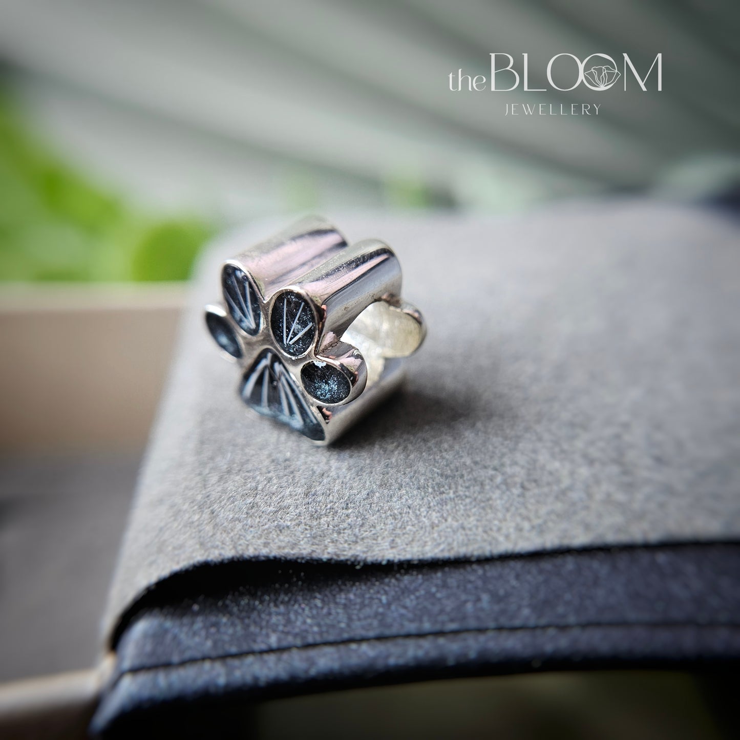 Silver charm with keepsake gemstones and fur on a gray surface, branded 'the BLOOM JEWELLERY'.