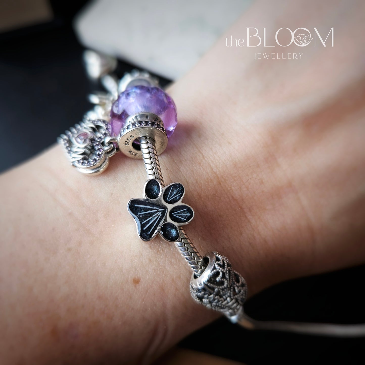 Silver bracelet with paw print charm on wrist, 'the BLOOM Jewellery' brand visible
