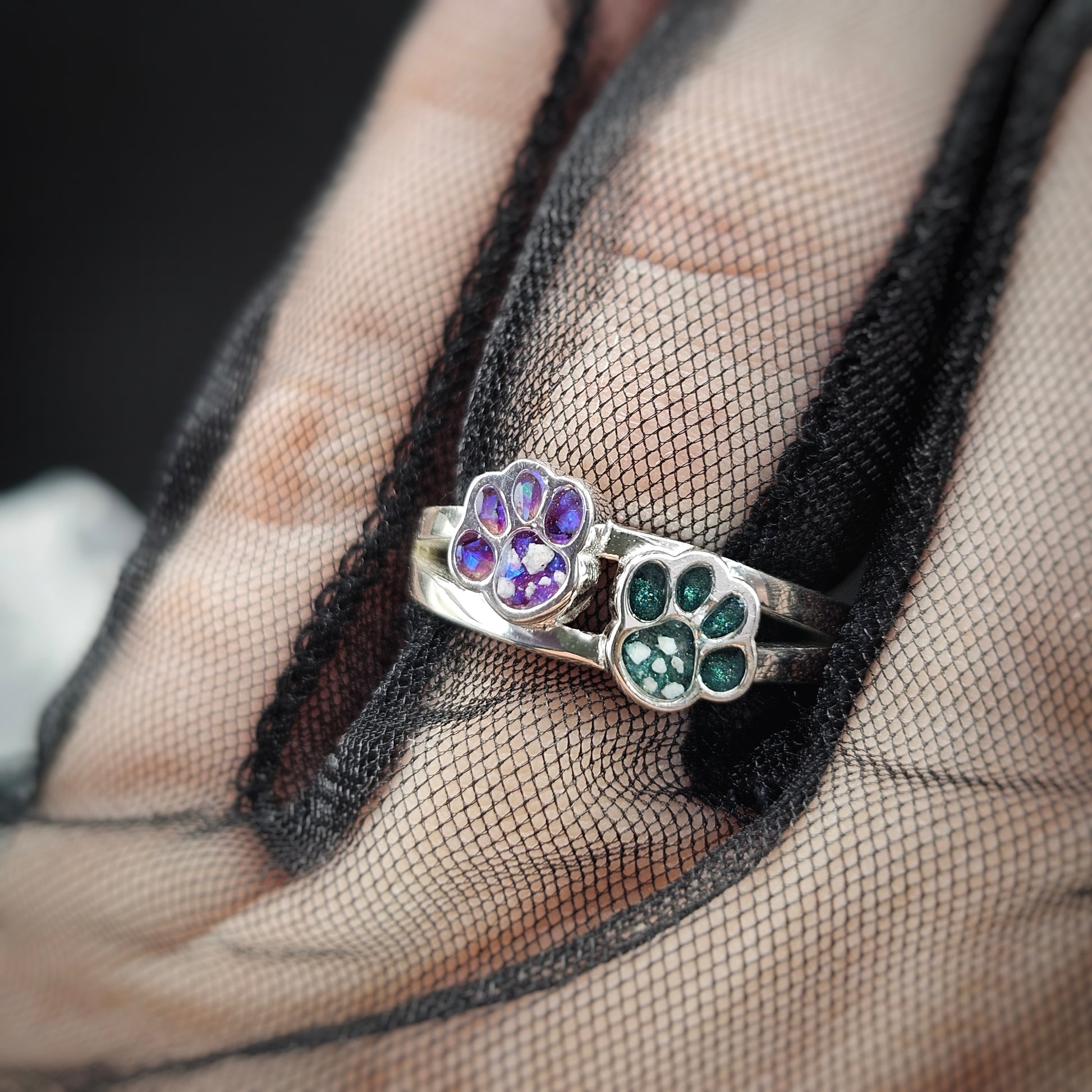 Two paw-shaped rings with colored stones on a hand wearing a black mesh glove.