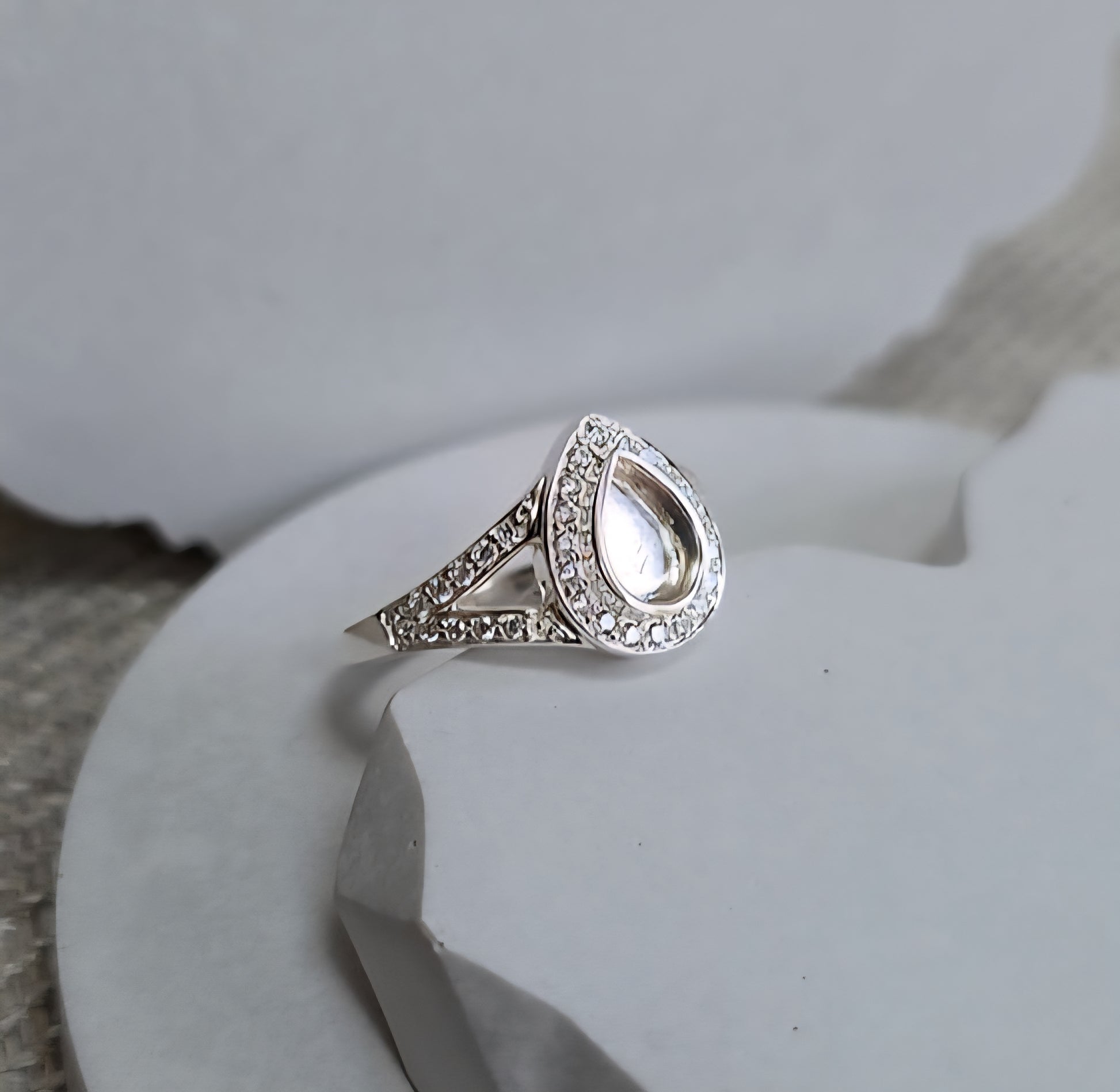 Silver teardrop ring with embedded stones on a white surface