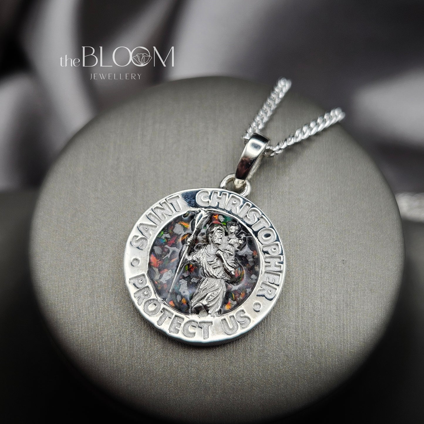 Silver Saint Christopher pendant on a gray surface with 'theBLOOM Jewellery' branding.