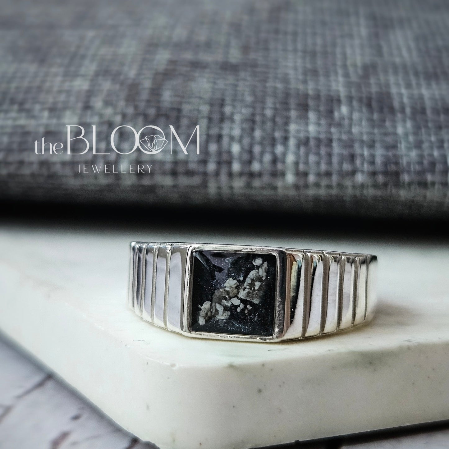 Silver ring with a black gemstone on a white surface, blurred background