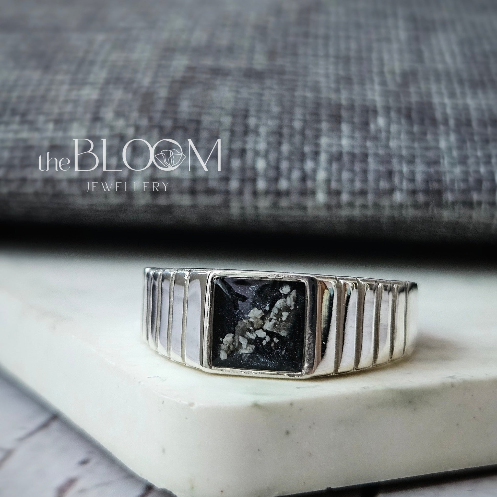 Silver ring with a black gemstone on a white surface, blurred background