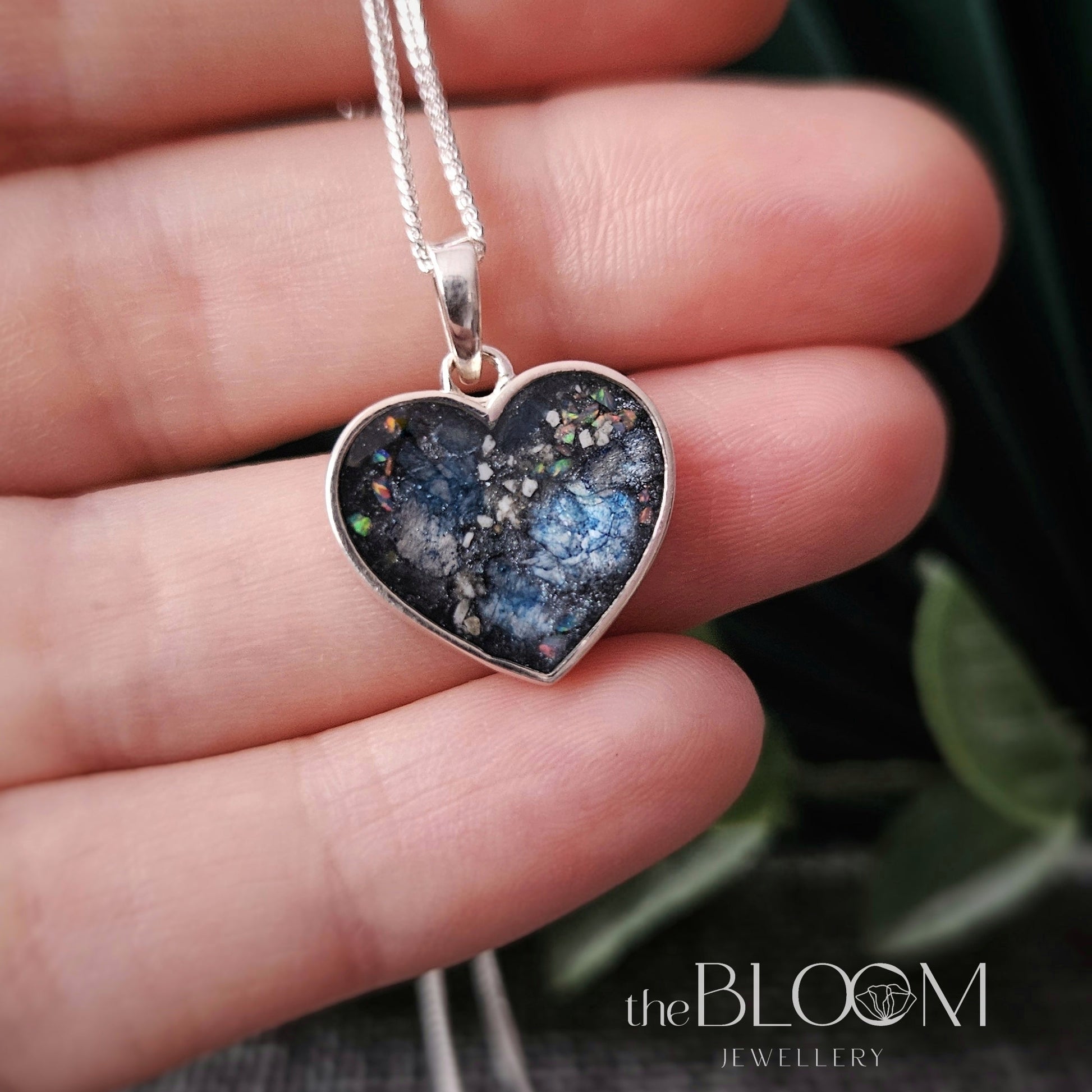 Heart-shaped pendant with a blue and black druzy design held in a hand.