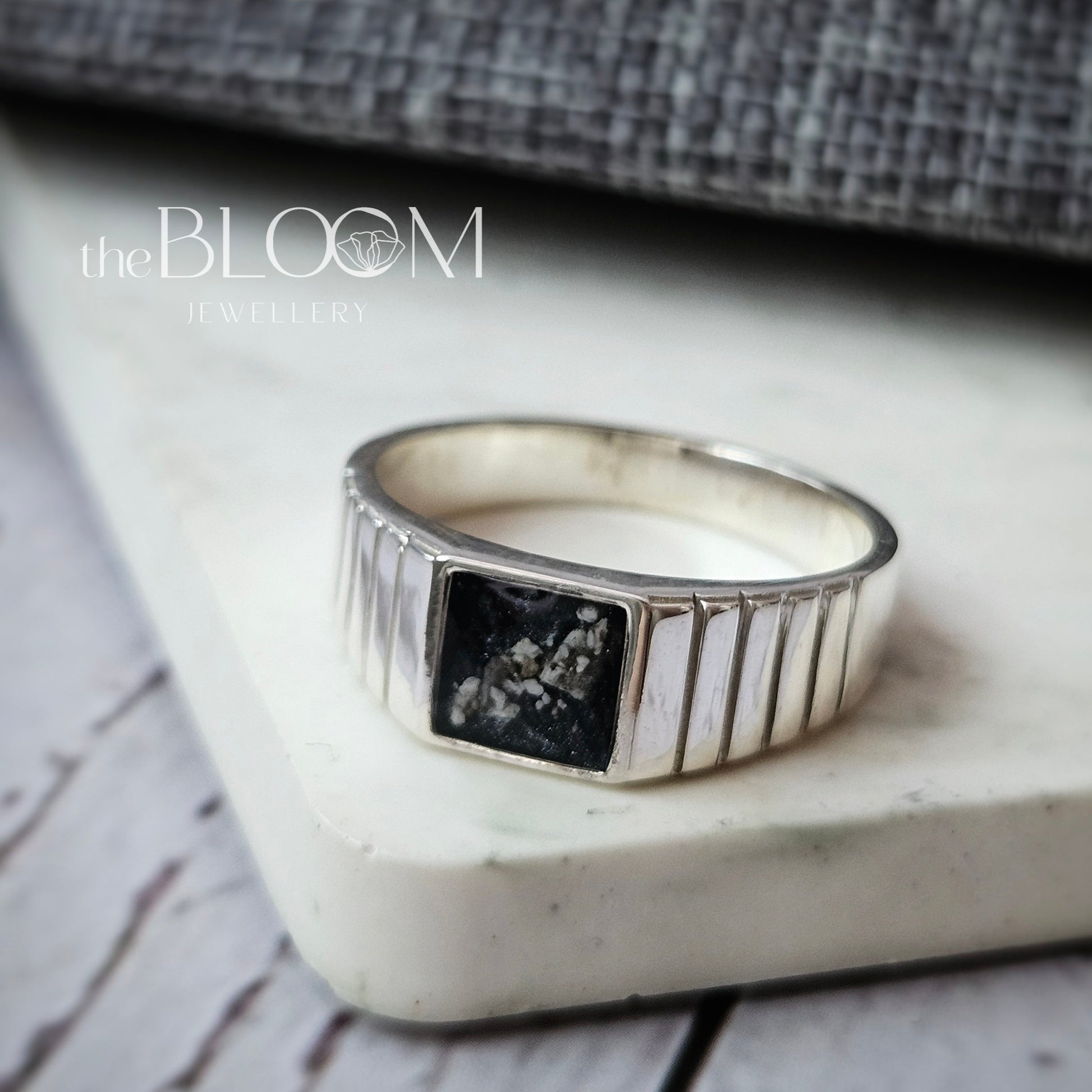Silver ring with a black stone on a marble stand with a textured gray fabric background.