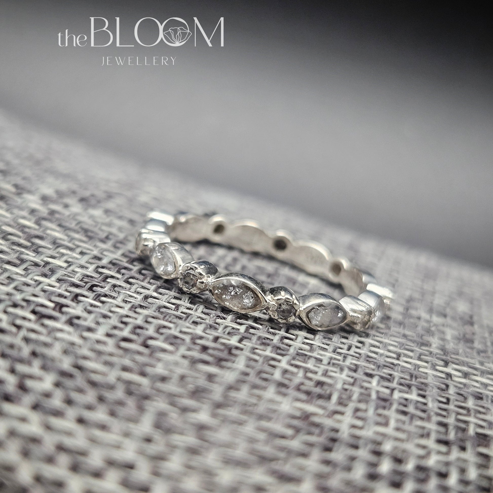 Silver ring with small stones on a textured fabric surface, branded 'the BLOOM Jewellery'.