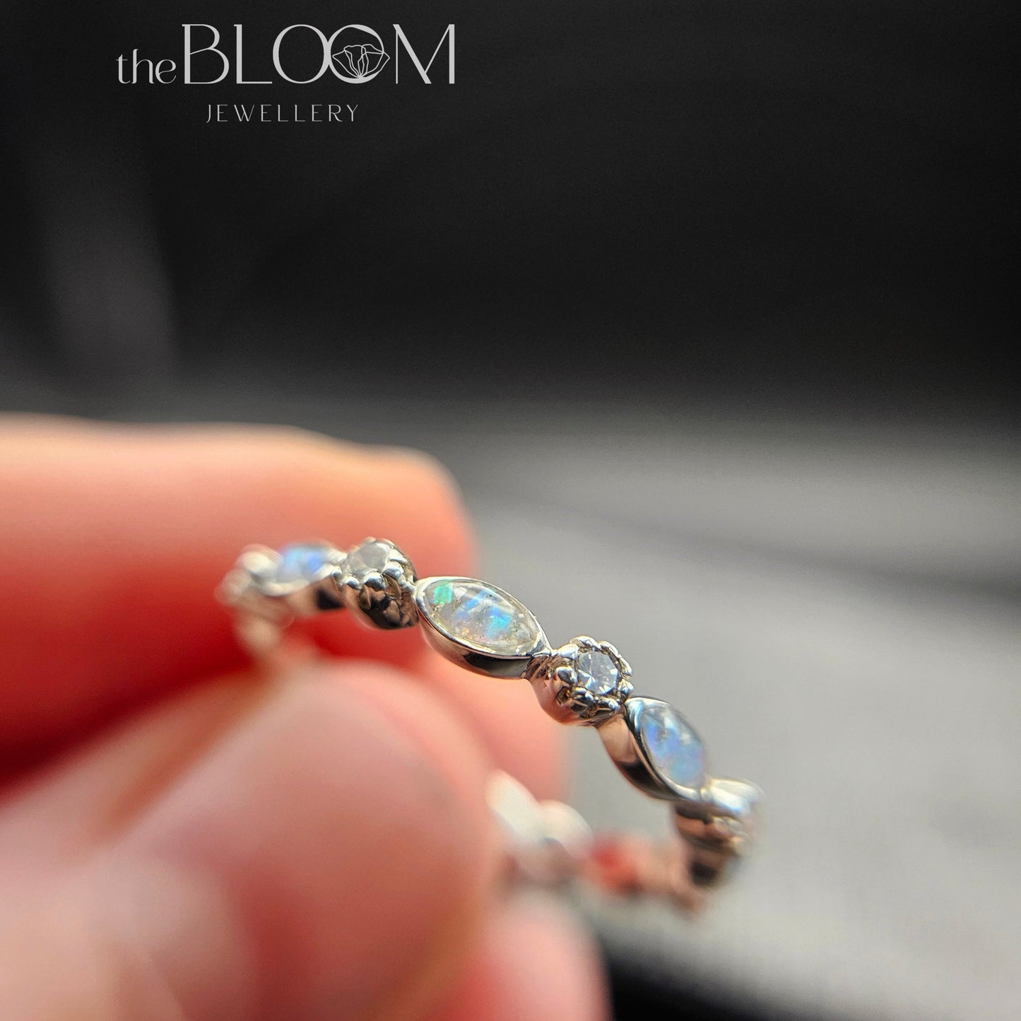 Silver ring with gemstones held by a hand, branded 'the BLOOM Jewellery'.