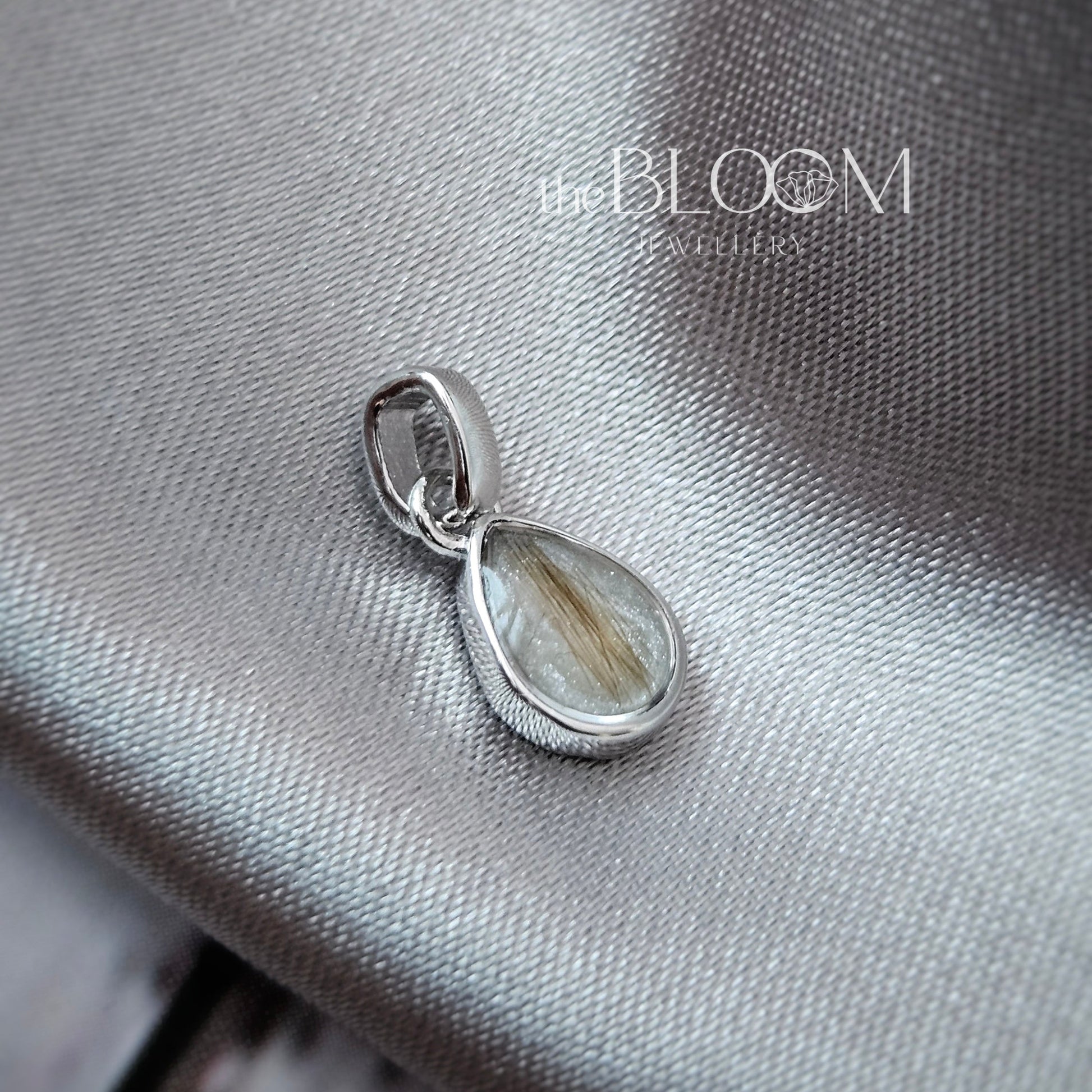 Silver pendant on a textured gray surface with 'The Bloom' brand visible.