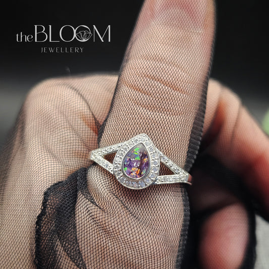 Silver ring with a purple gemstone held by a hand wearing a sheer glove, branded 'the BLOOM JEWELLERY'.
