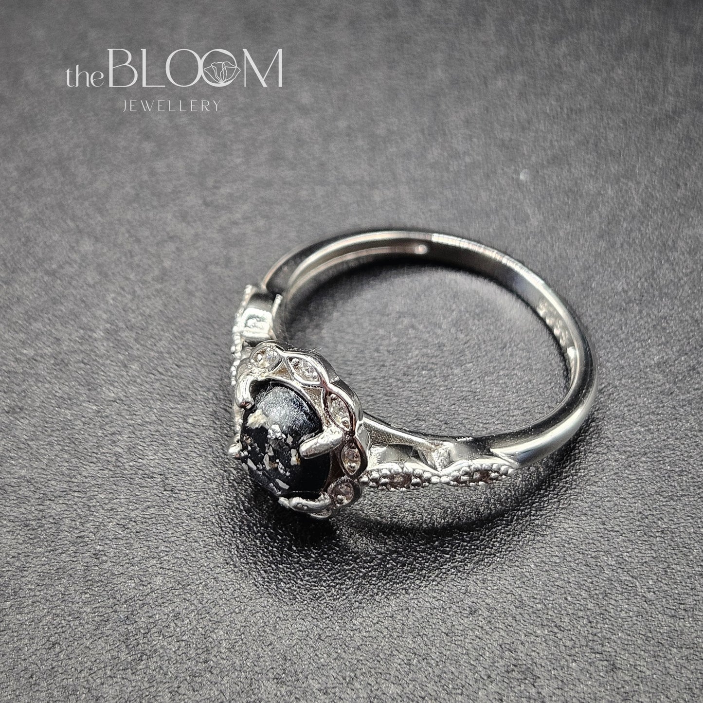 Silver ring with a dark gemstone on a gray background, branded 'the BLOOM Jewellery'.