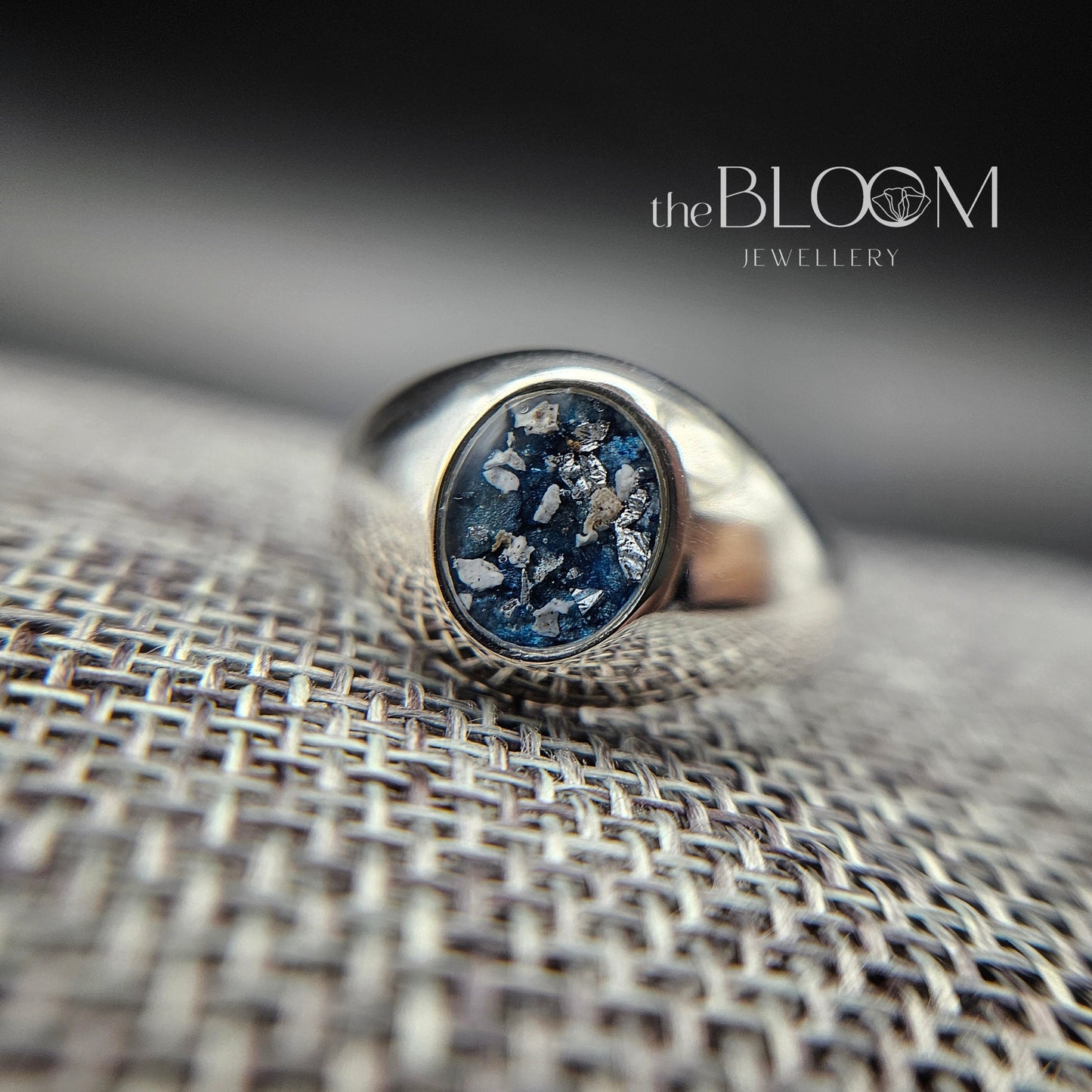 Silver ring with blue stone on a textured surface, branded 'the BLOOM Jewellery'.