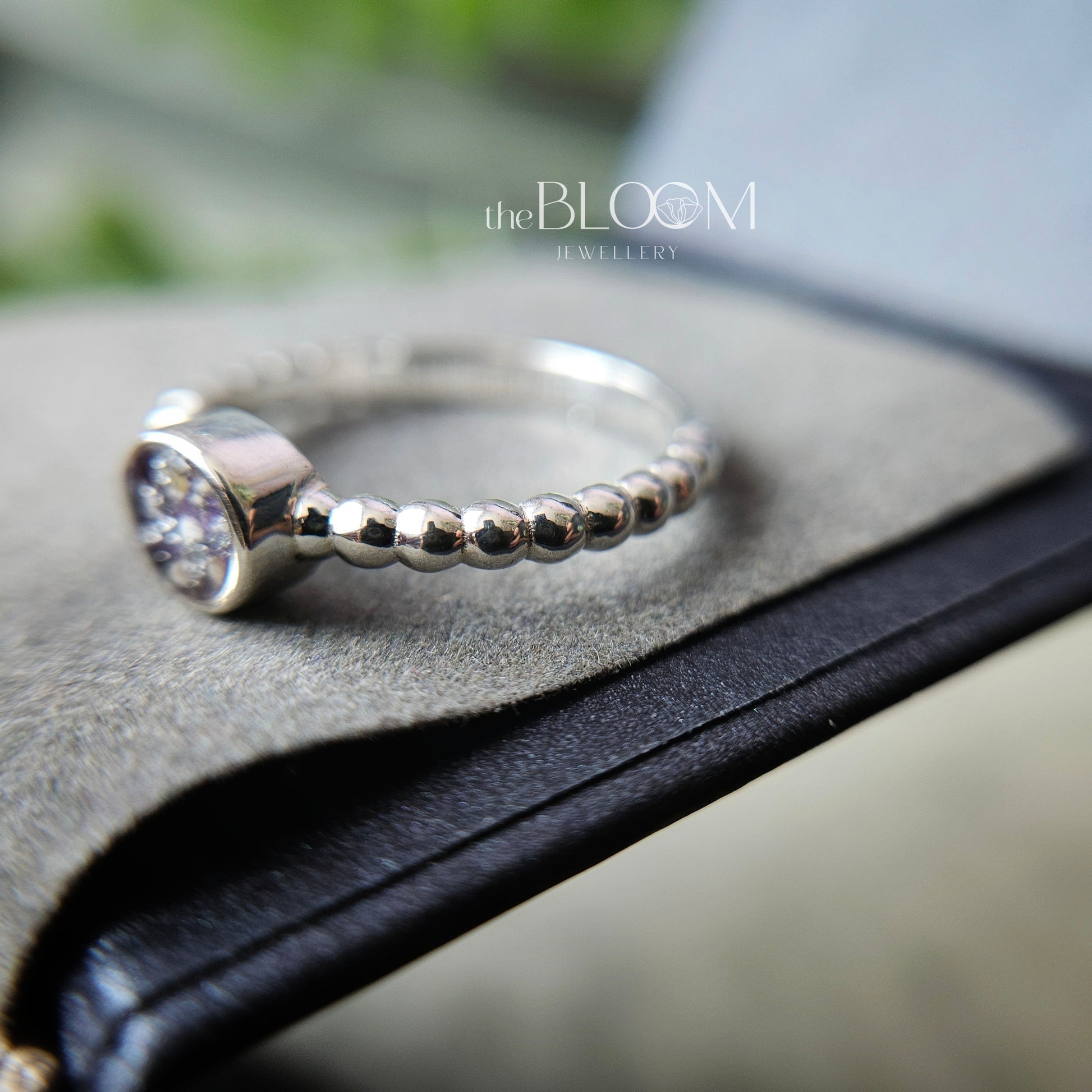 Silver ring with a diamond on a black leather surface, branded 'the BLOOM Jewellery'.
