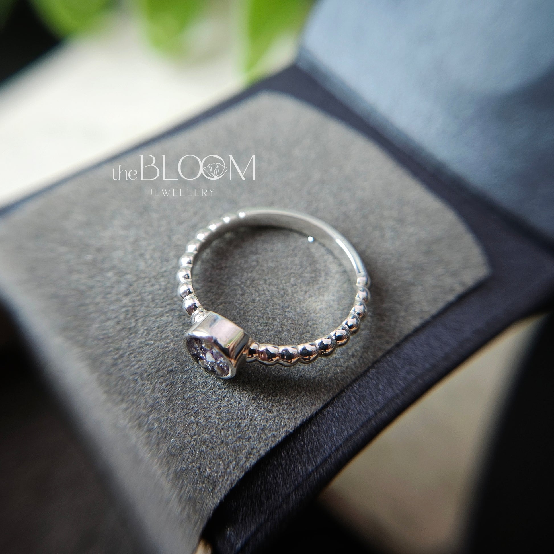 Silver ring with a diamond on a gray surface, branded 'the BLOOM Jewellery'.