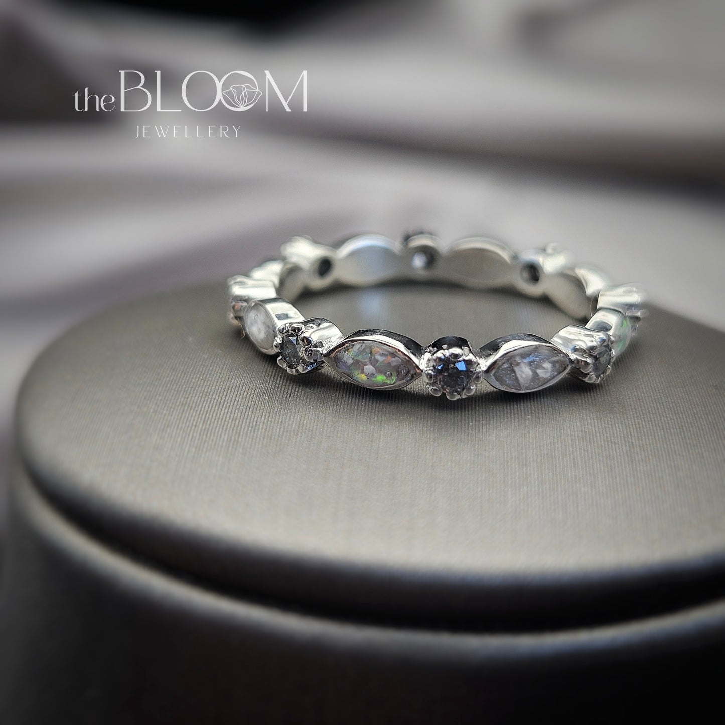 Silver ring with gemstones on a gray surface, branded 'the BLOOM JEWELLERY'.