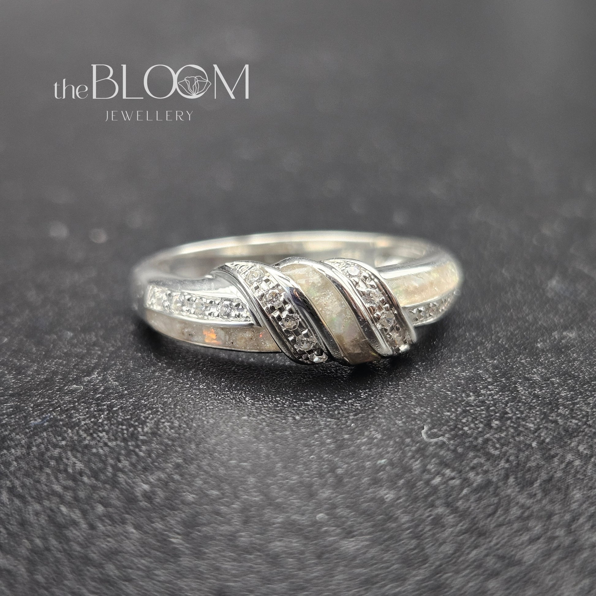 Silver ring with diamond accents on a dark textured surface, branded 'the BLOOM Jewellery'.