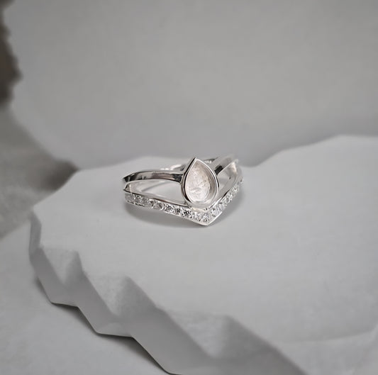 Silver ring with a teardrop design and small diamonds on a light gray background