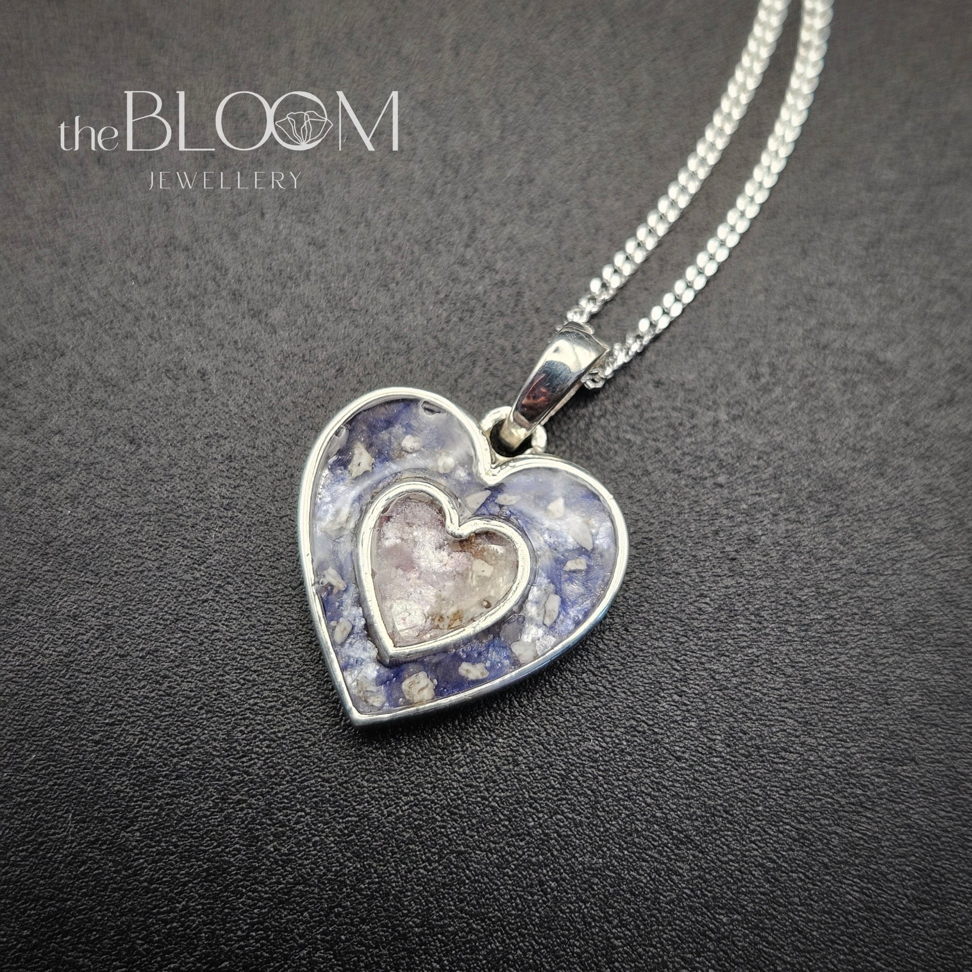 Heart-shaped silver pendant with embedded stones on a dark background, branded 'the BLOOM Jewellery'.
