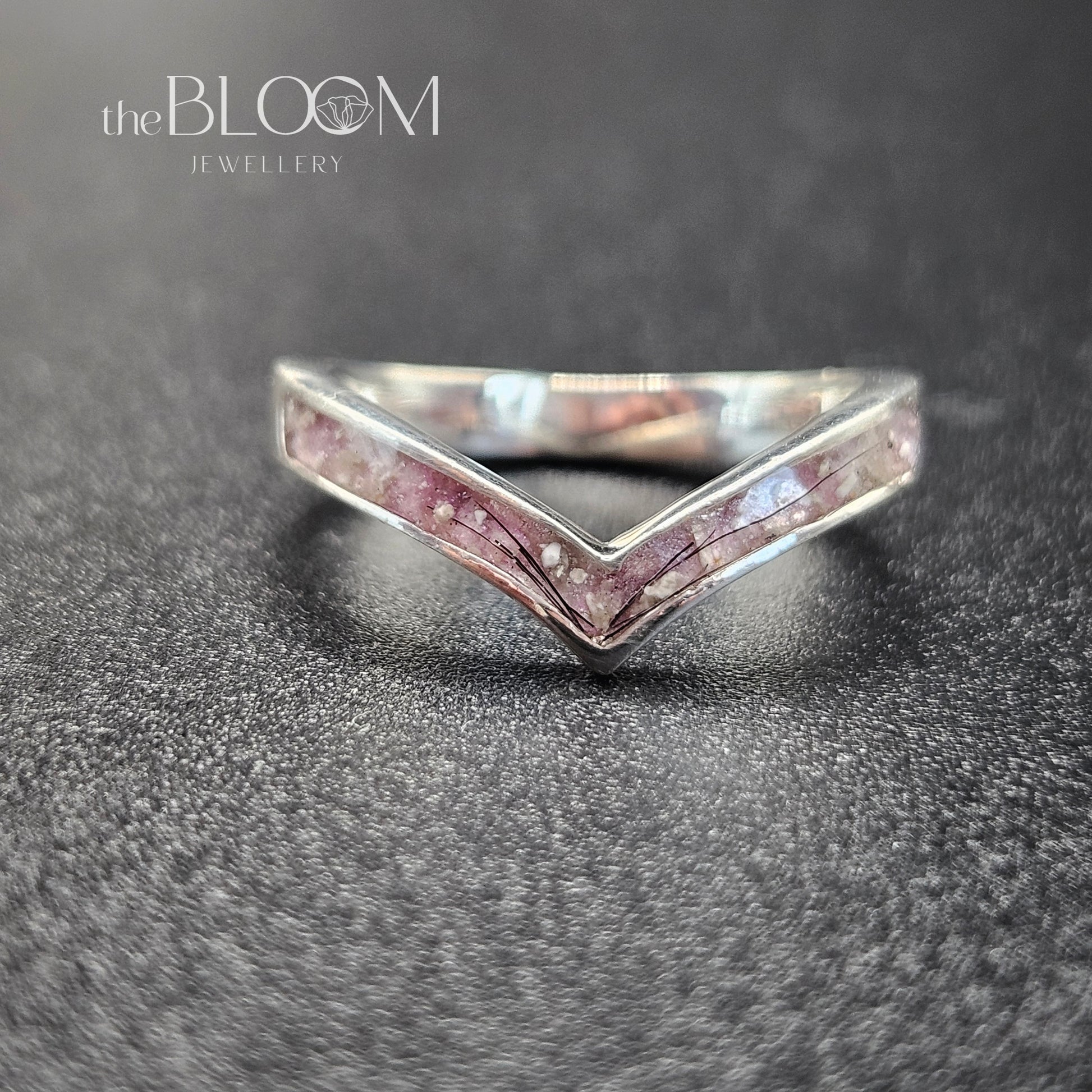 Silver ring with pink gemstones on a dark textured surface, branded 'the BLOOM Jewellery'.
